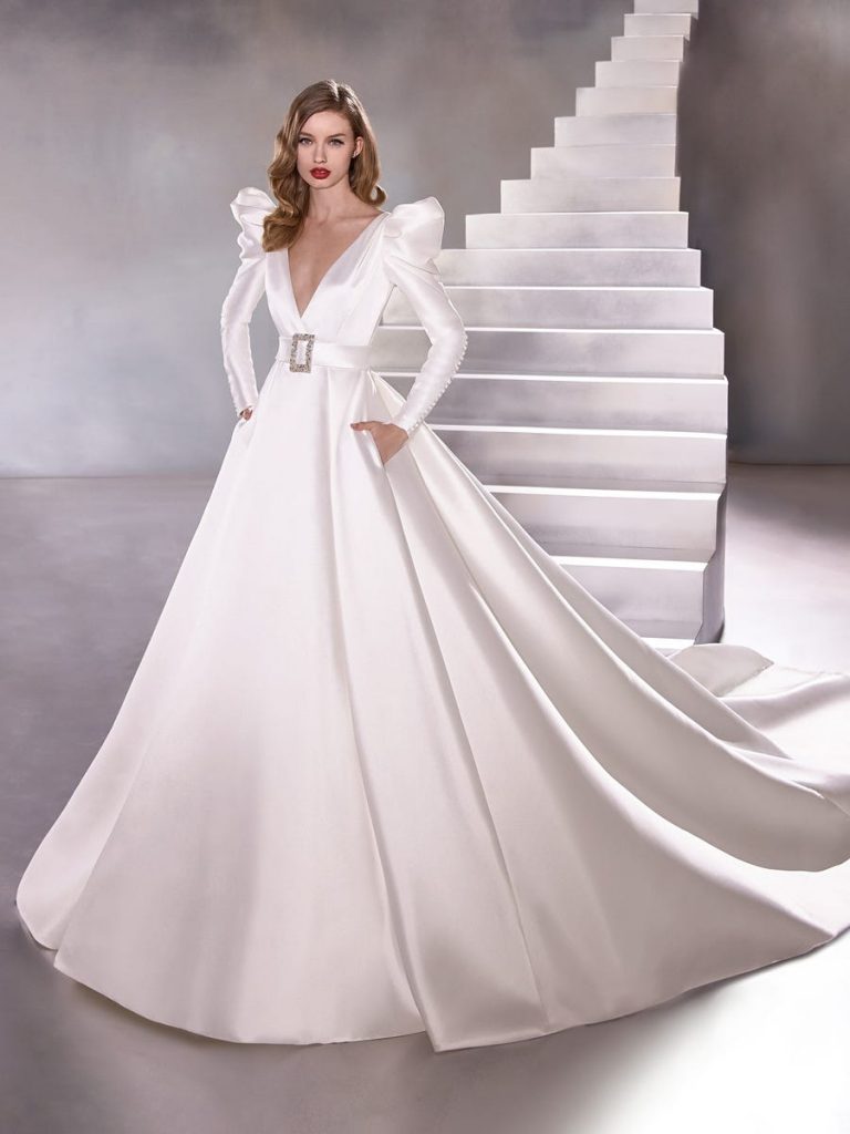 Winter wedding gown with 80s shoulders, long sleeves and buttons up to the elbow, belted waist and ball gown skirt.